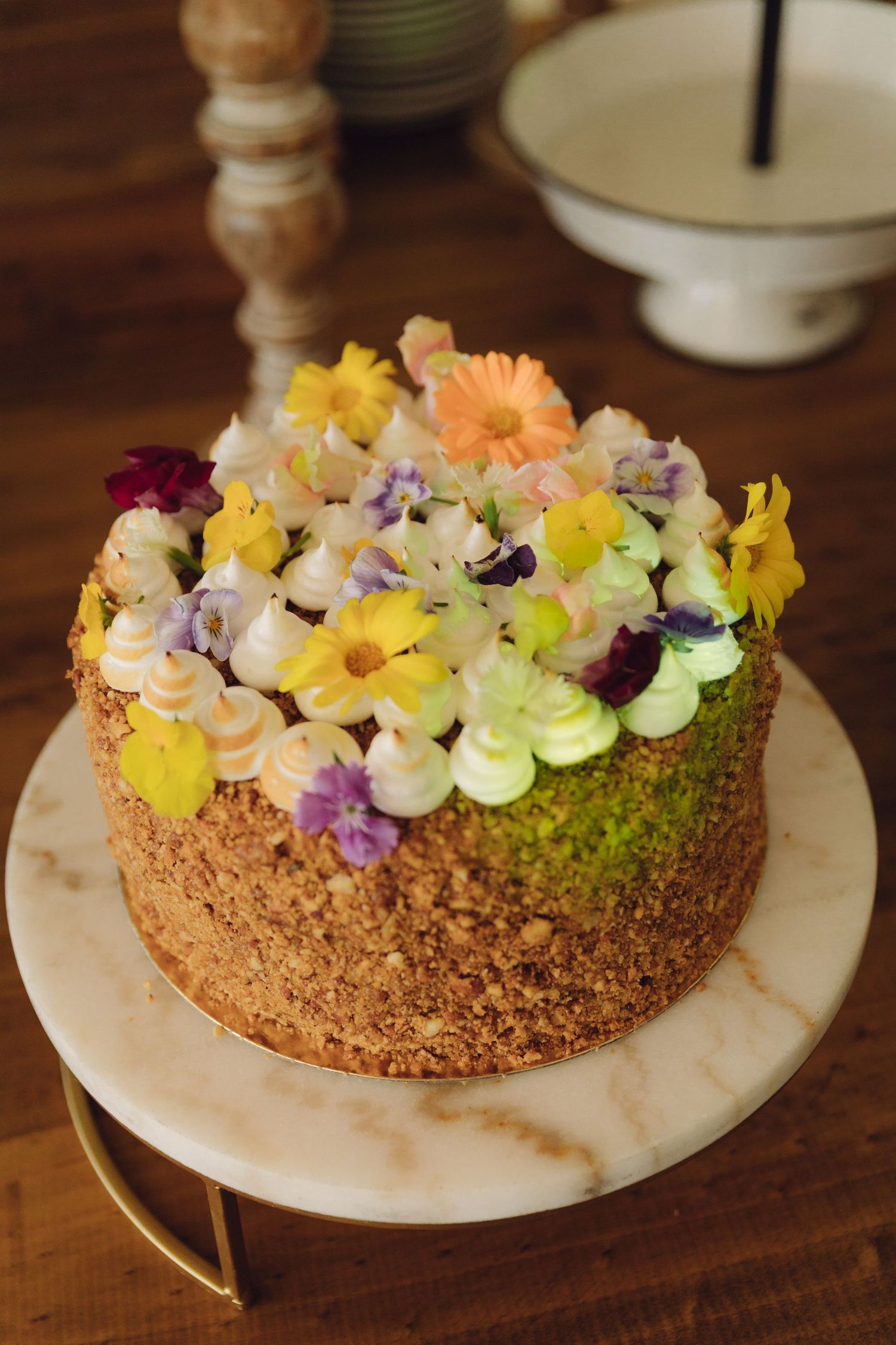 Rustic wedding cake decorated with colorful edible flowers on a marble stand.