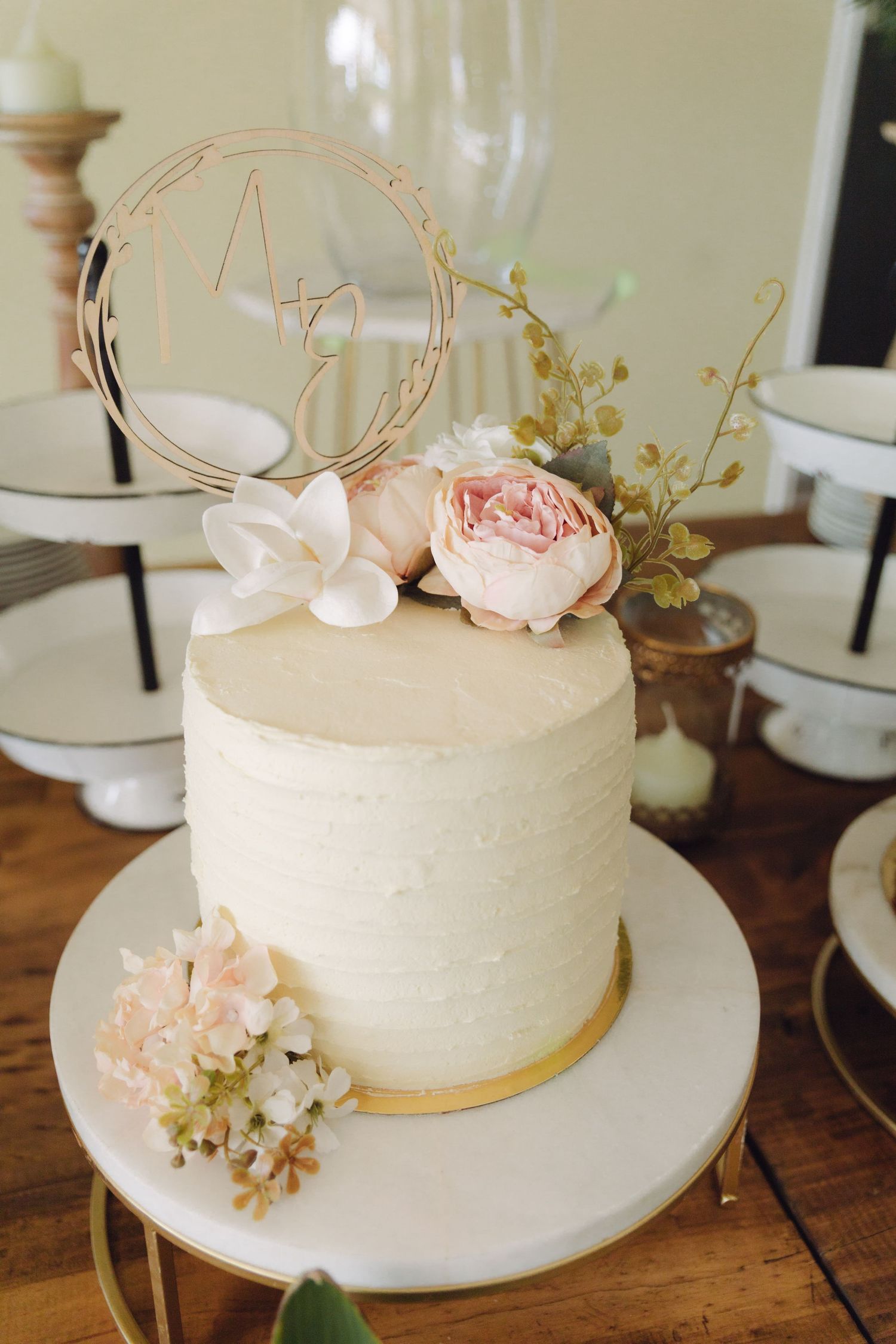 Elegant single-tier white wedding cake with pink roses and gold trim on marble stand.