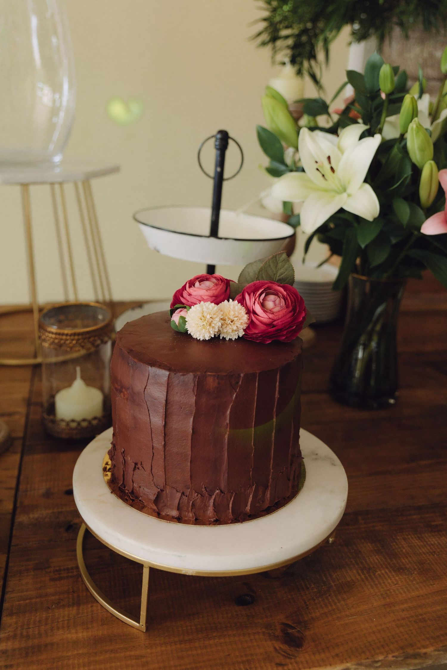 Rich chocolate wedding cake decorated with pink and white flowers on a marble cake stand.