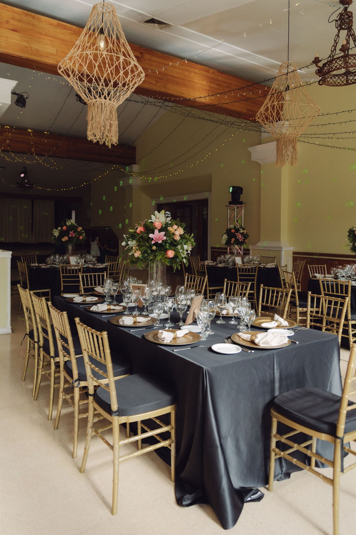Elegant wedding reception hall with dark tablecloths, gold chiavari chairs, and floral centerpieces.