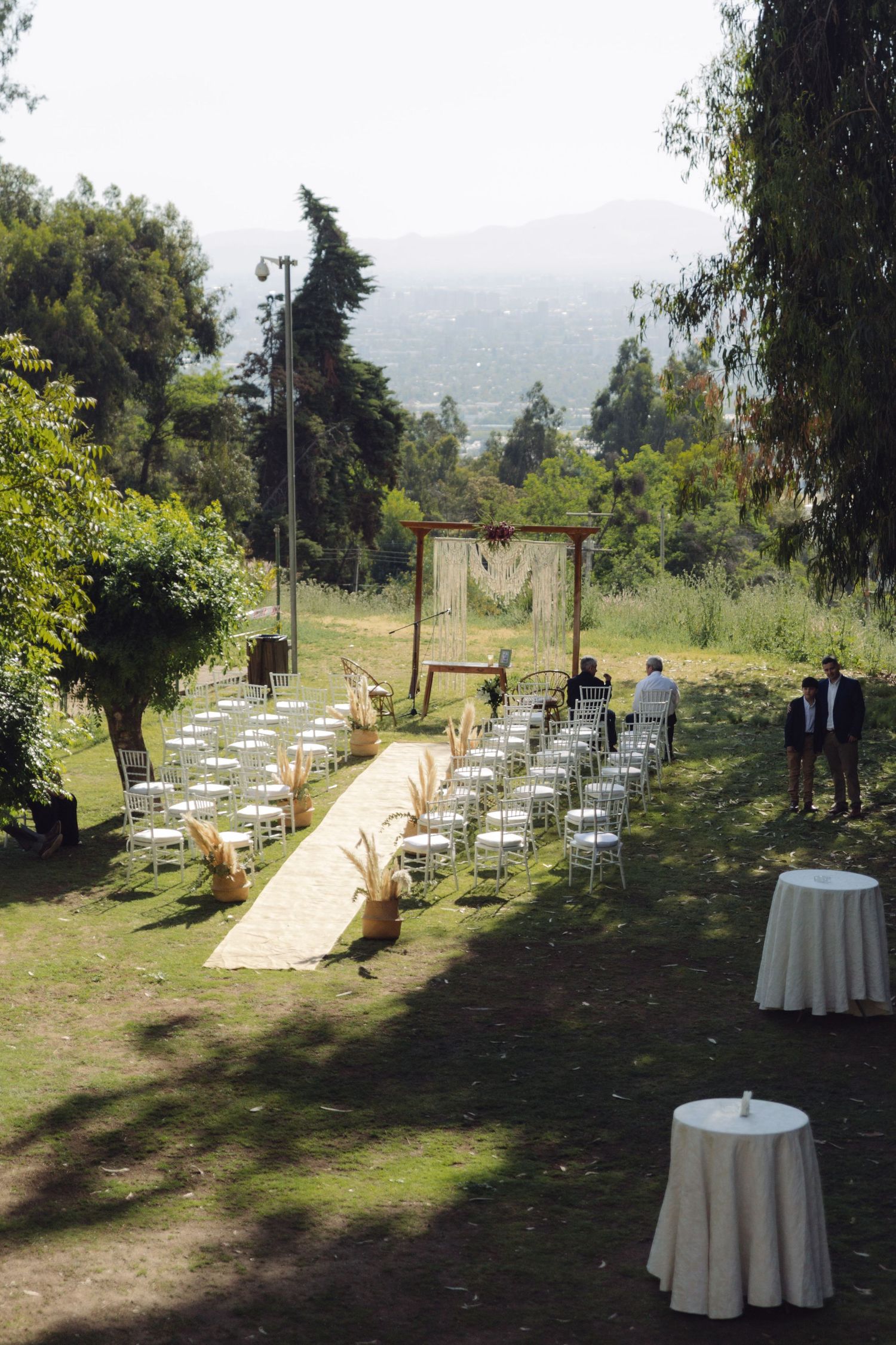 Outdoor wedding ceremony setup with white chairs, yellow aisle runner, wooden arch, and scenic mountain backdrop.