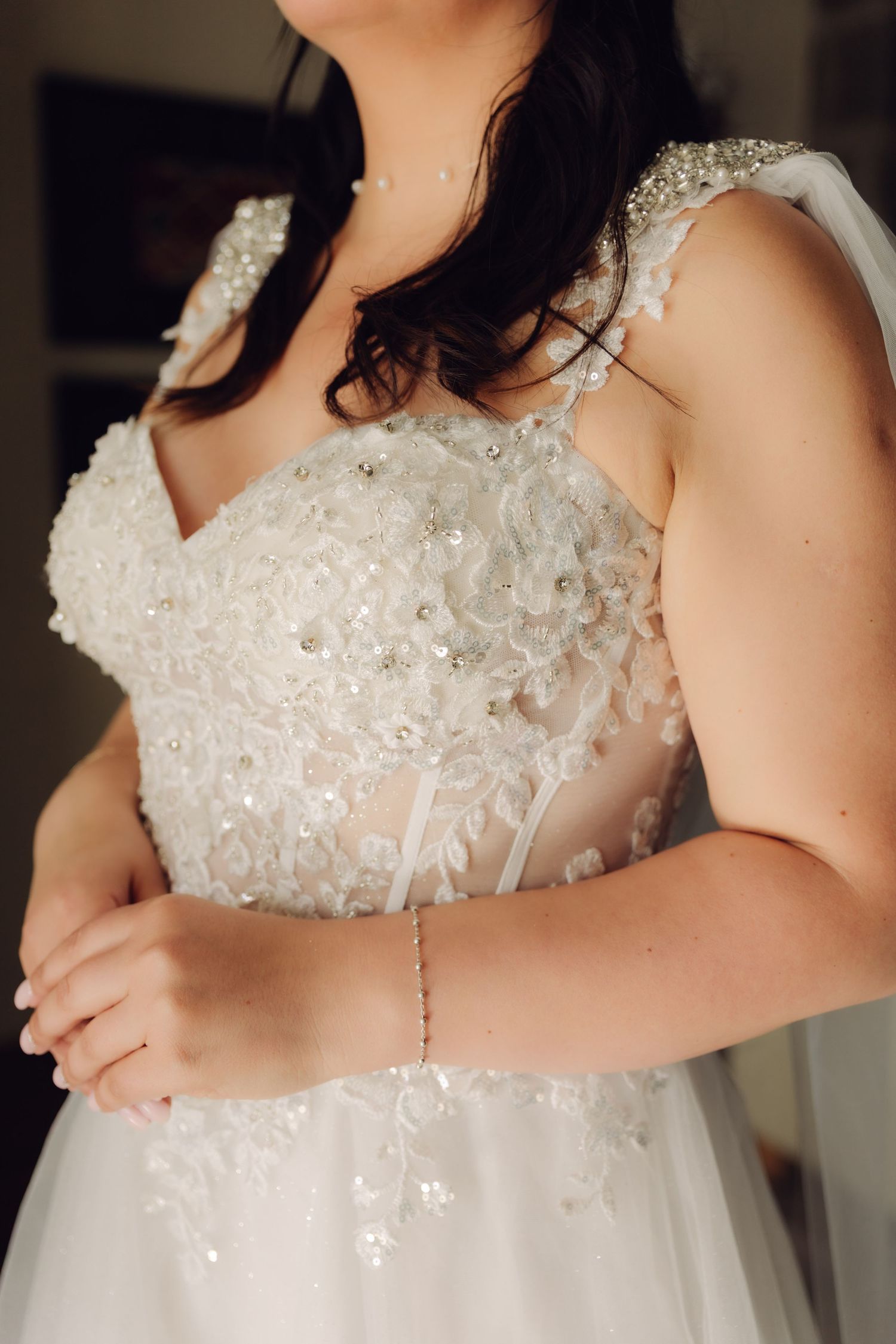 Detail shot of brides lace and crystal embellished wedding dress bodice with delicate bracelet and veil strap.