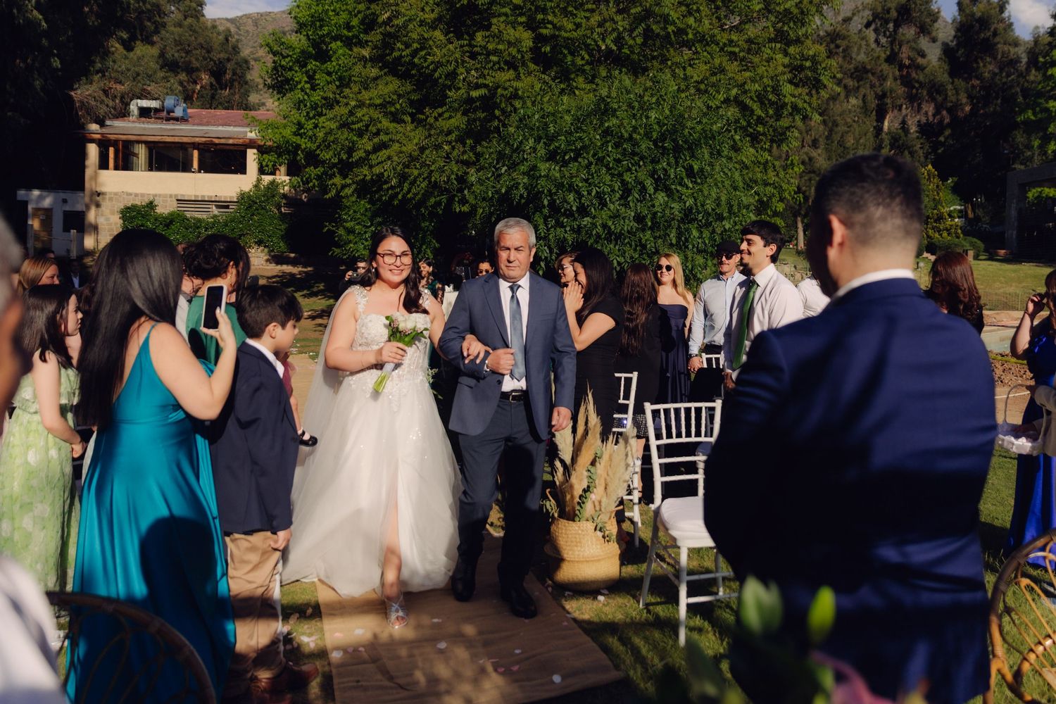 Bride walks down outdoor aisle with escort at garden wedding ceremony.