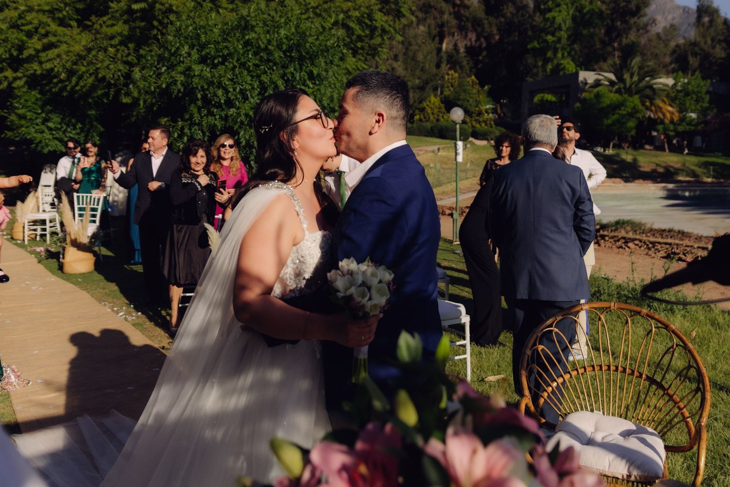 Newlyweds share first kiss at outdoor garden wedding ceremony.