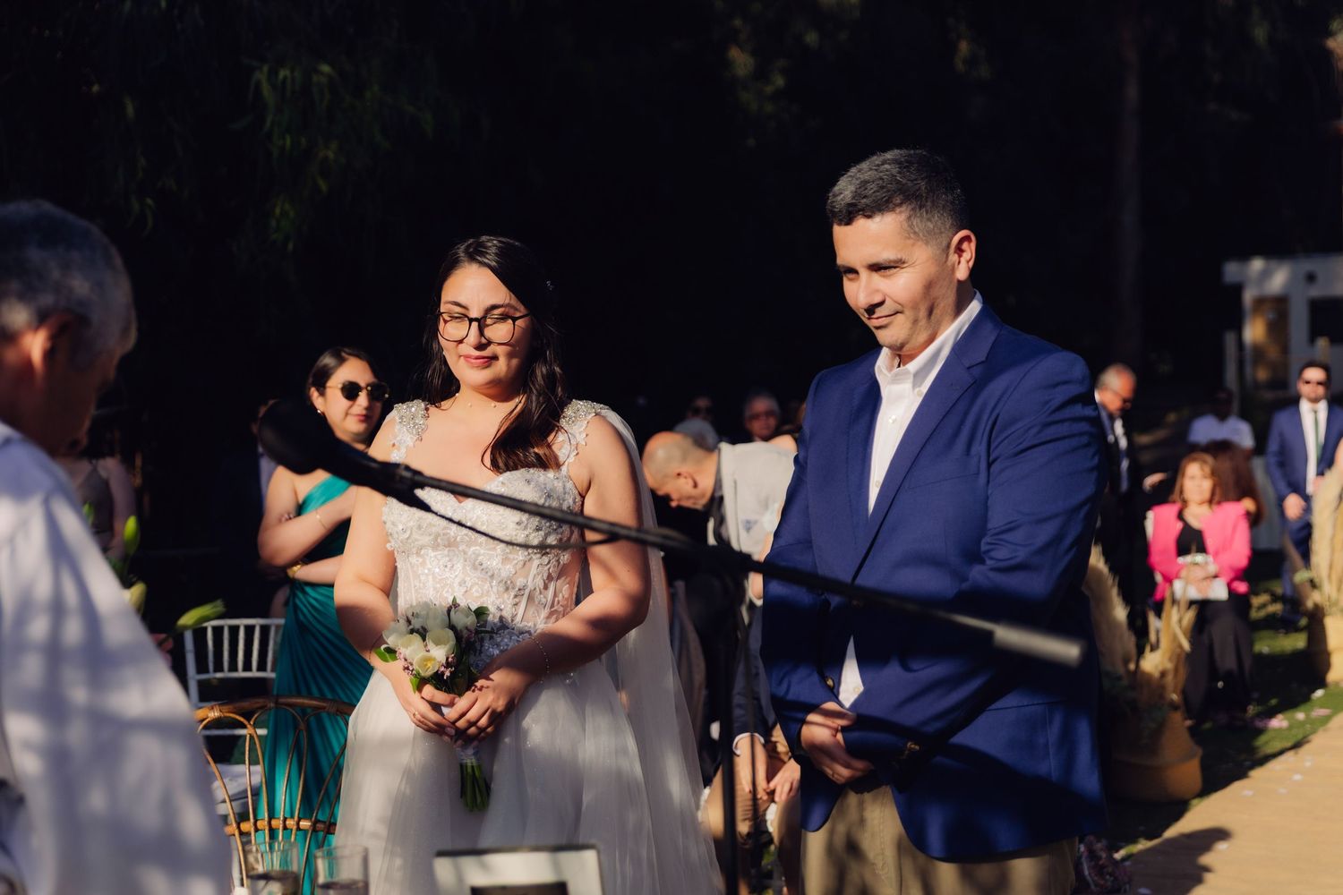 Smiling bride and groom stand together during outdoor wedding ceremony.