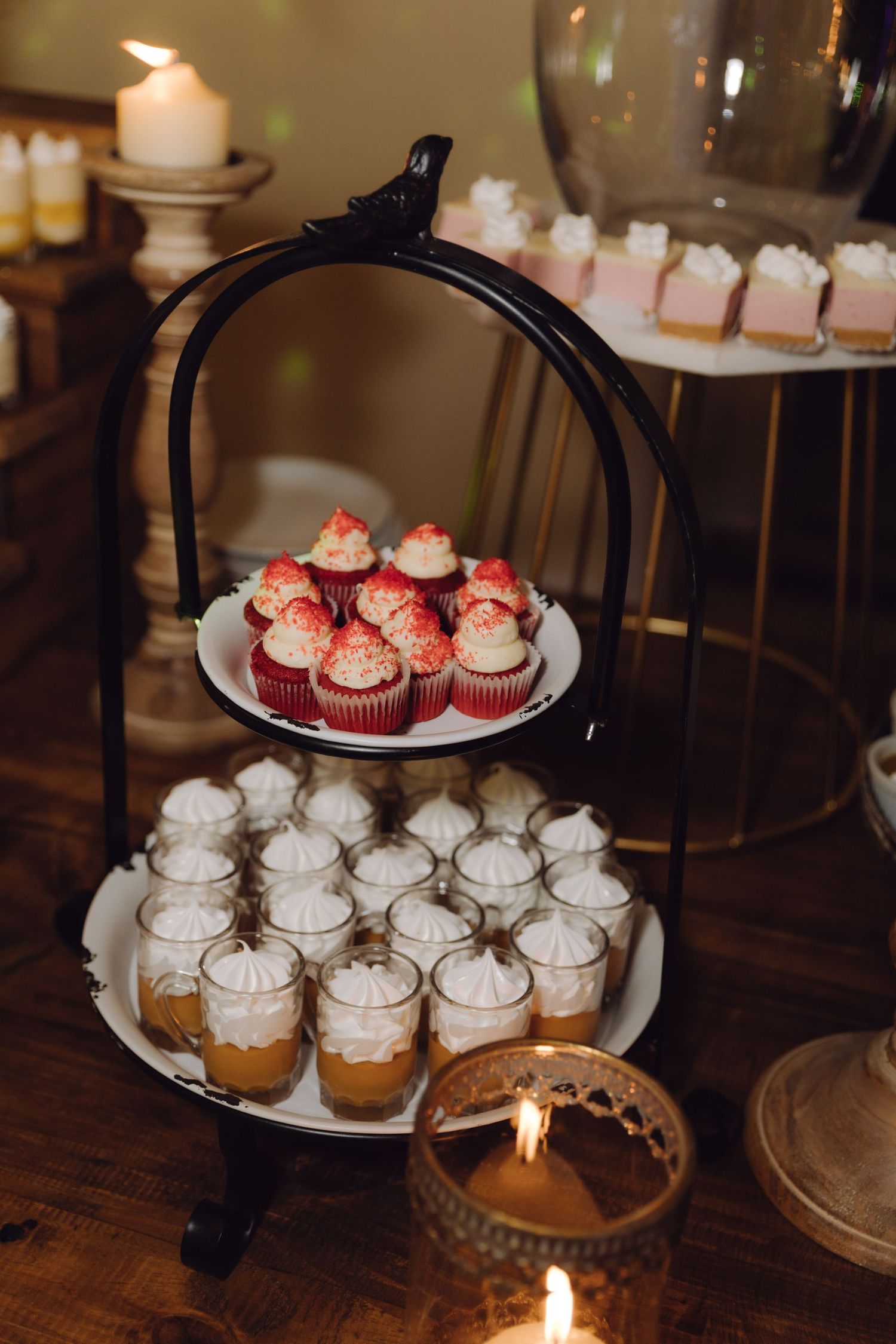 Two-tiered black metal dessert stand with red velvet cupcakes and caramel mousse cups at wedding reception.