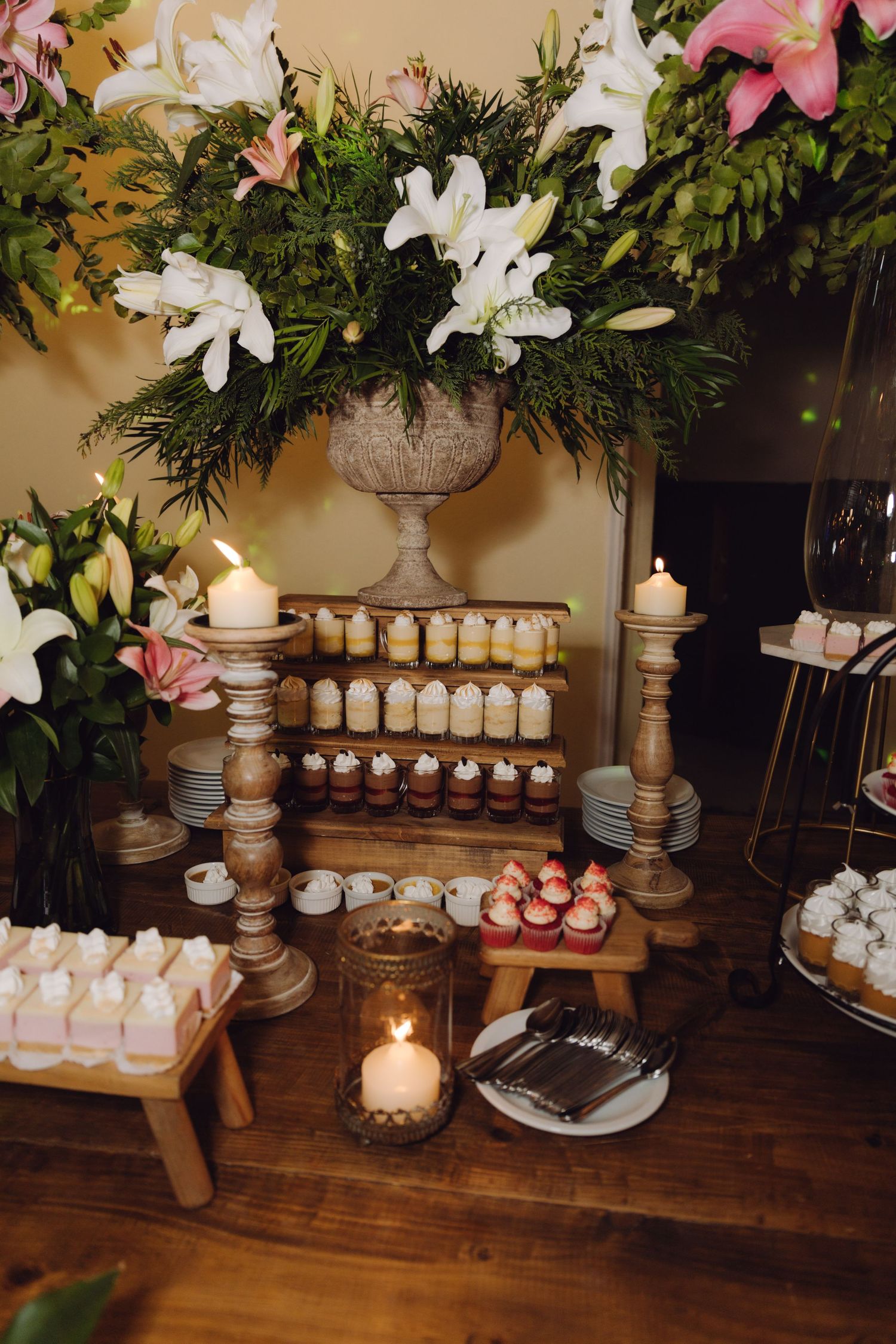 Wedding candy bar featuring tiered dessert display, lit candles, white lily bouquet, and assorted sweet treats.