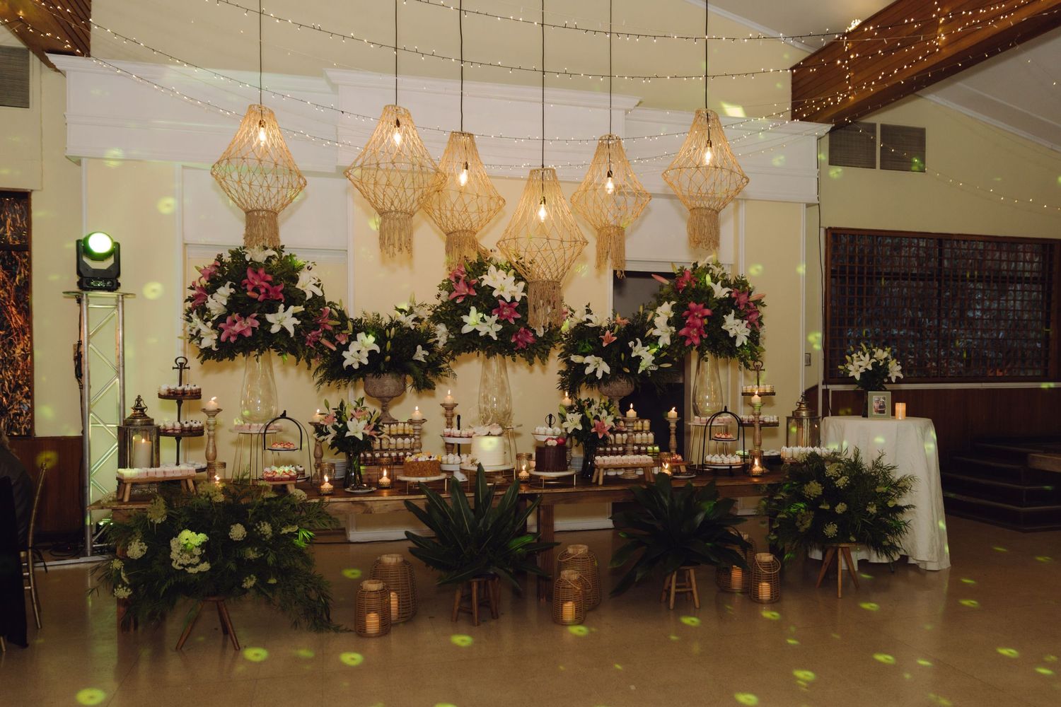 Wedding reception dessert table with macrame pendant lights, floral arrangements, and elegant decorative displays.
