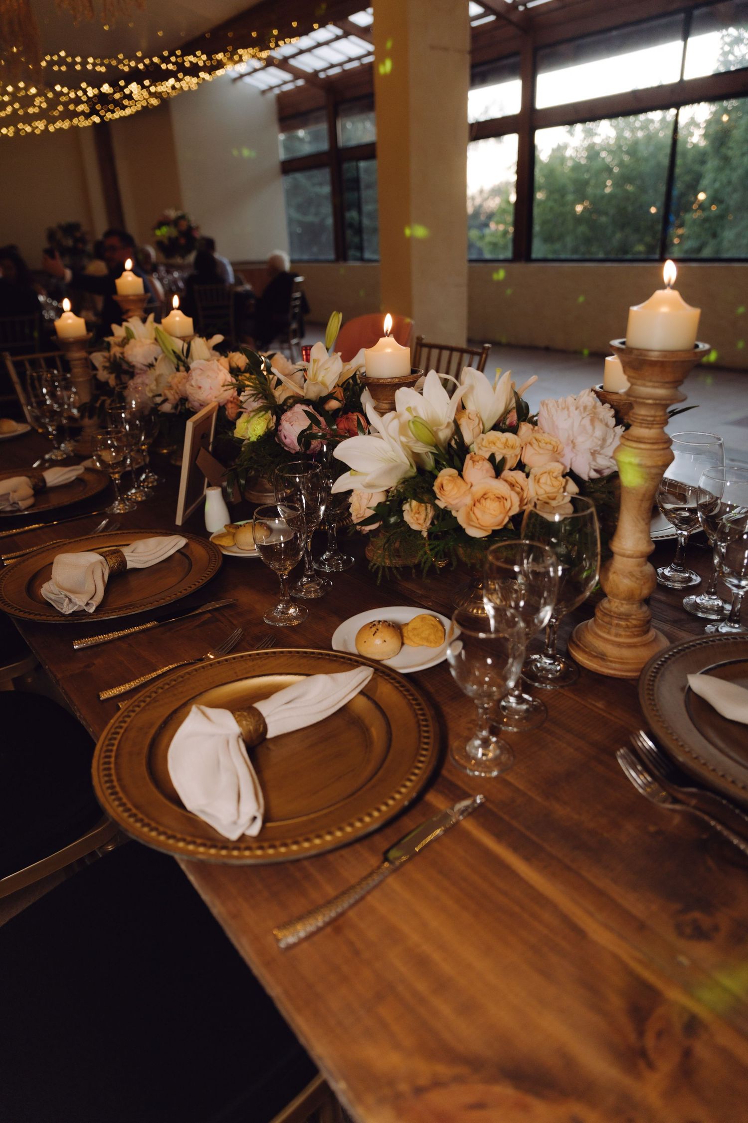 Elegant wedding table setting with gold charger plates, white napkins, candles, and pink floral centerpieces.