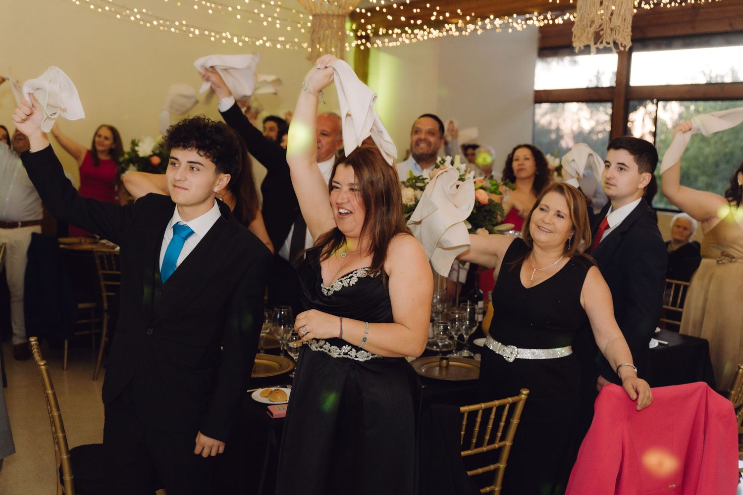 Excited wedding guests waving white napkins in celebration at an elegant indoor reception venue.