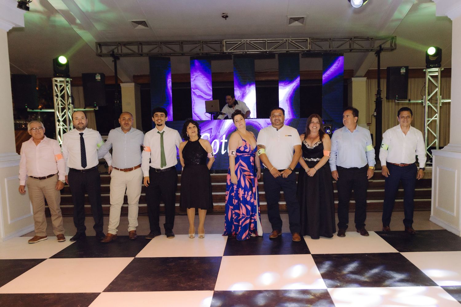 Group of elegantly dressed wedding guests posing together on a black and white checkered dance floor at a reception.