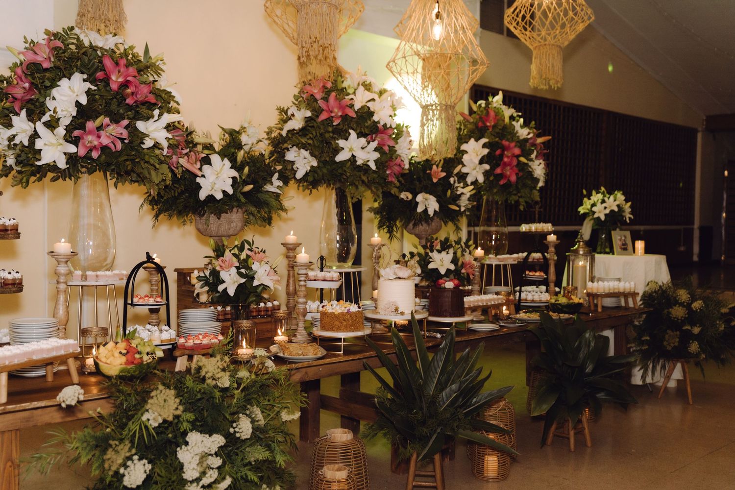 Elegant wedding dessert table adorned with tall floral arrangements of white lilies, pink flowers, and candles.