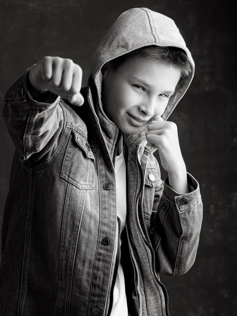 Close-up black and white portrait of a confident school-age boy wearing a hooded denim jacket like a boxer at professional studio session.