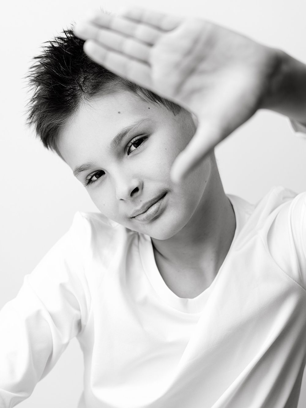Creative black and white portrait of a smiling school-age boy framing his face with his hand during a studio back to school photoshoot.