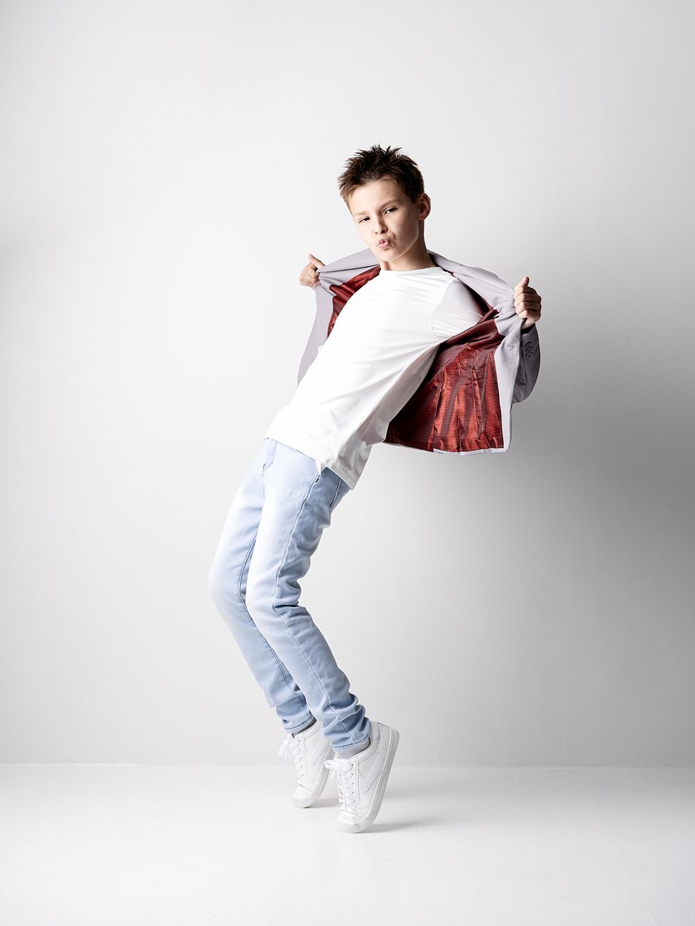 Creative portrait of a playful school-age boy opening his blazer during a fun back-to-school photoshoot.