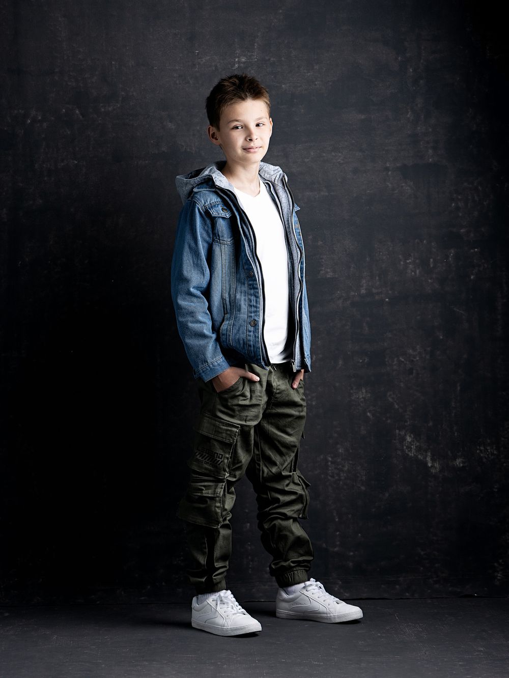 Full-length portrait of a smiling school-age boy in casual clothes photographed in a professional studio before the new school year.