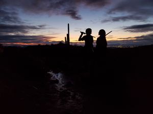 Silhouettes of two children against a dramatic dusk sky with saguaro cactus on the horizon in the Arizona desert.