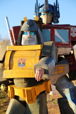 Close-up of a Bumblebee-style Transformers costume with an Autobot emblem and Optimus Prime costume standing behind it.