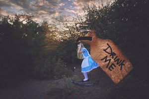 Alice in a blue dress stands beside a giant bottle labeled Drink Me in a forest at sunset, in a whimsical Wonderland scene.