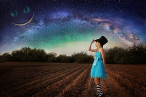 Girl in a blue dress, top hat and striped socks stands in a plowed field gazing at a colorful Milky Way sky with a Cheshire cat grin moon.