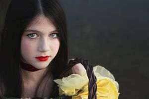 Close-up portrait of a dark-haired girl with red lipstick and a red choker holding a basket of yellow roses.