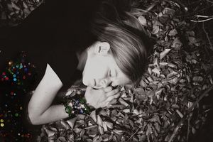 A black and white portrait of a woman resting her head on her hands among fallen leaves, with colorful sparkling lights glowing nearby.