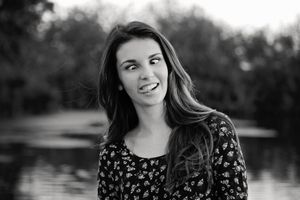 Black and white portrait of a playful young woman with long hair making a silly face and sticking out her tongue by a lake.