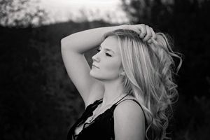 Black and white profile portrait of a woman with long wavy hair and one hand raised to her head.