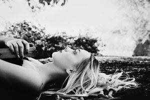 Black and white portrait of a woman with long blonde hair lying on the ground with her head tilted back, eyes closed.