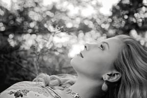 Black and white portrait of a woman lying back and gazing upward with sparkling bokeh light behind her.