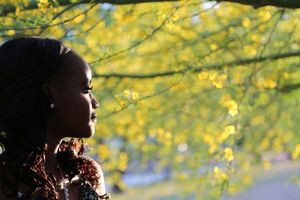 Side profile of a woman gazing into the distance beside tree branches covered in bright yellow blossoms.