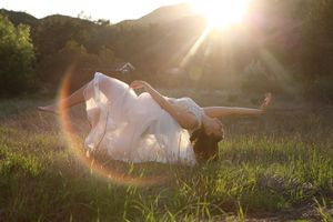 Woman in a white dress appears to float above a green meadow while golden sunlight and lens flare glow behind her.