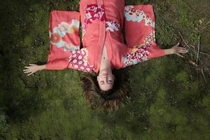Overhead view of a woman in a coral floral kimono lying on mossy green grass with her arms outstretched and her hair spread.