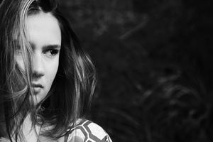 Black and white close-up portrait of a young woman with windswept hair partly covering her face, looking intently to the side.