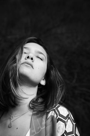 Black-and-white portrait of a young woman tilting her head back with closed eyes, wearing layered necklaces and a patterned kimono.