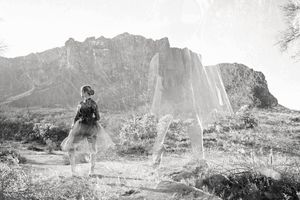 A black and white double-exposure photo of a dancer in a tutu on a desert trail with rugged mountains behind her.