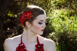 Close-up portrait of a young woman with red flowers in her hair and on her top, in profile with red lipstick.