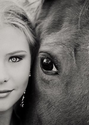 Black and white portrait of a young woman with light eyes beside the large dark eye of a horse.