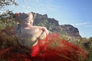 Double exposure portrait of a woman in a flowing red skirt blended with a rugged mountain landscape and blue sky.