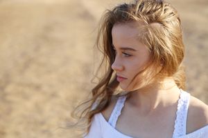 Young woman in a white top with windblown hair gazes into the distance against a soft golden sandy background.