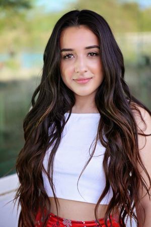 Portrait of a smiling young woman with long wavy dark hair wearing a white crop top outdoors.