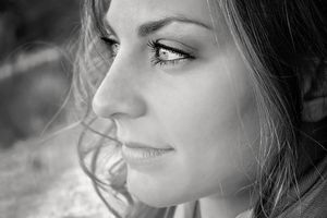 Black and white close-up portrait of a woman with wavy hair gazing softly into the distance with a gentle expression.
