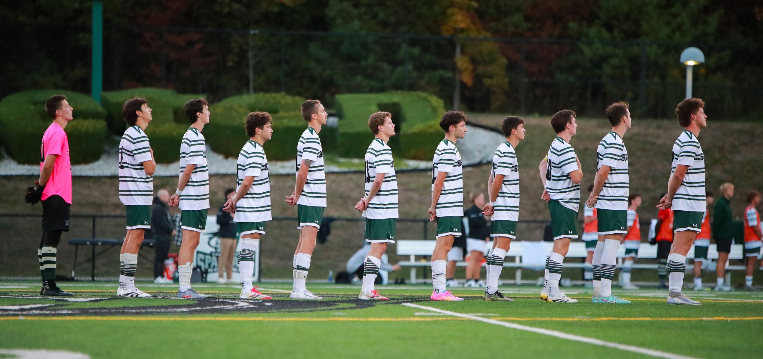 Field hockey players lined up in white striped uniforms before a match on a grass field.