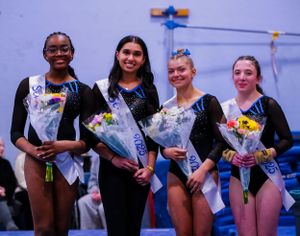 Gymnasts holding flower bouquets at an awards ceremony in black leotards.