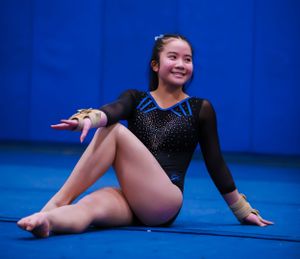 Gymnast striking graceful pose on blue competition mat during floor exercise.