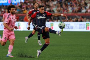 Soccer players battle for possession during competitive match on grass field.