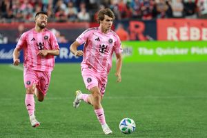 Soccer players in pink jerseys dribble the ball during a professional match on a grass field.