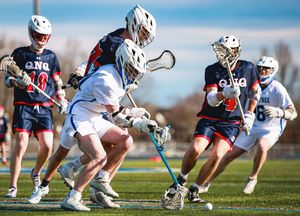 Lacrosse players face off at midfield during a competitive match on a sunny day.