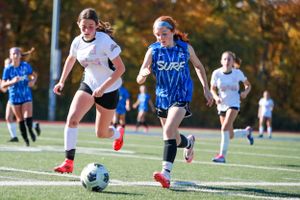 Youth soccer players running across field during competitive match in autumn.