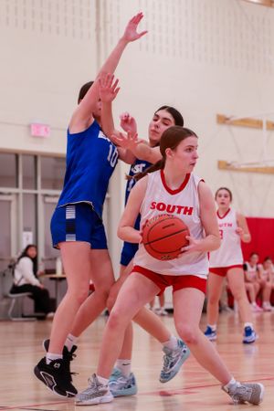 Basketball player protects the ball while defender attempts to block in an indoor game.
